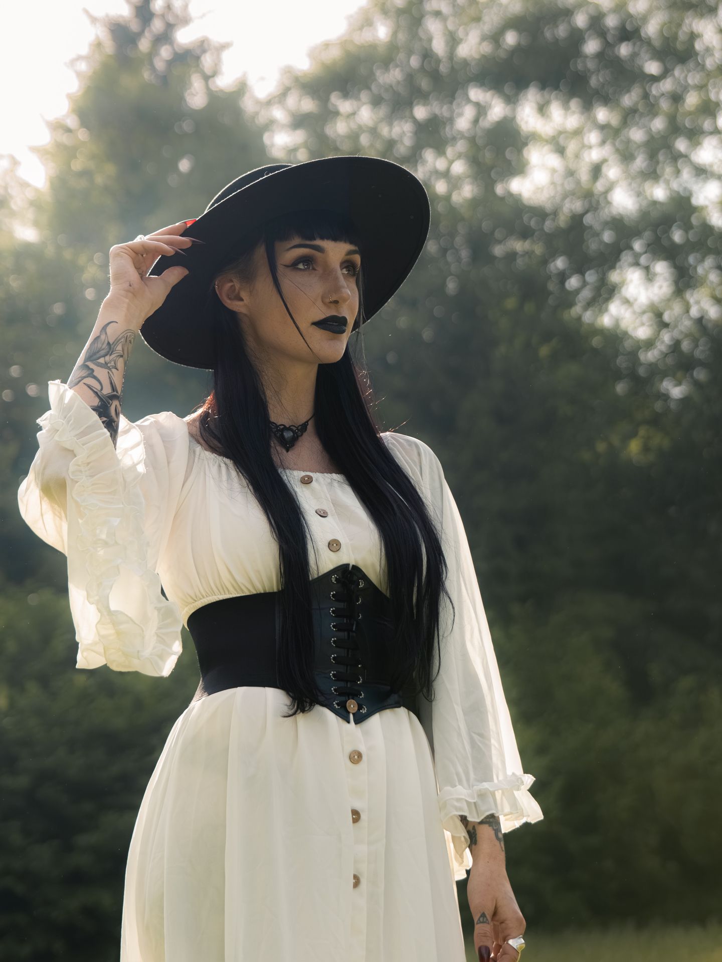 Eine Frau trägt ein weißes Kleid und einen schwarzen Hut in einem sonnigen Umfeld.
